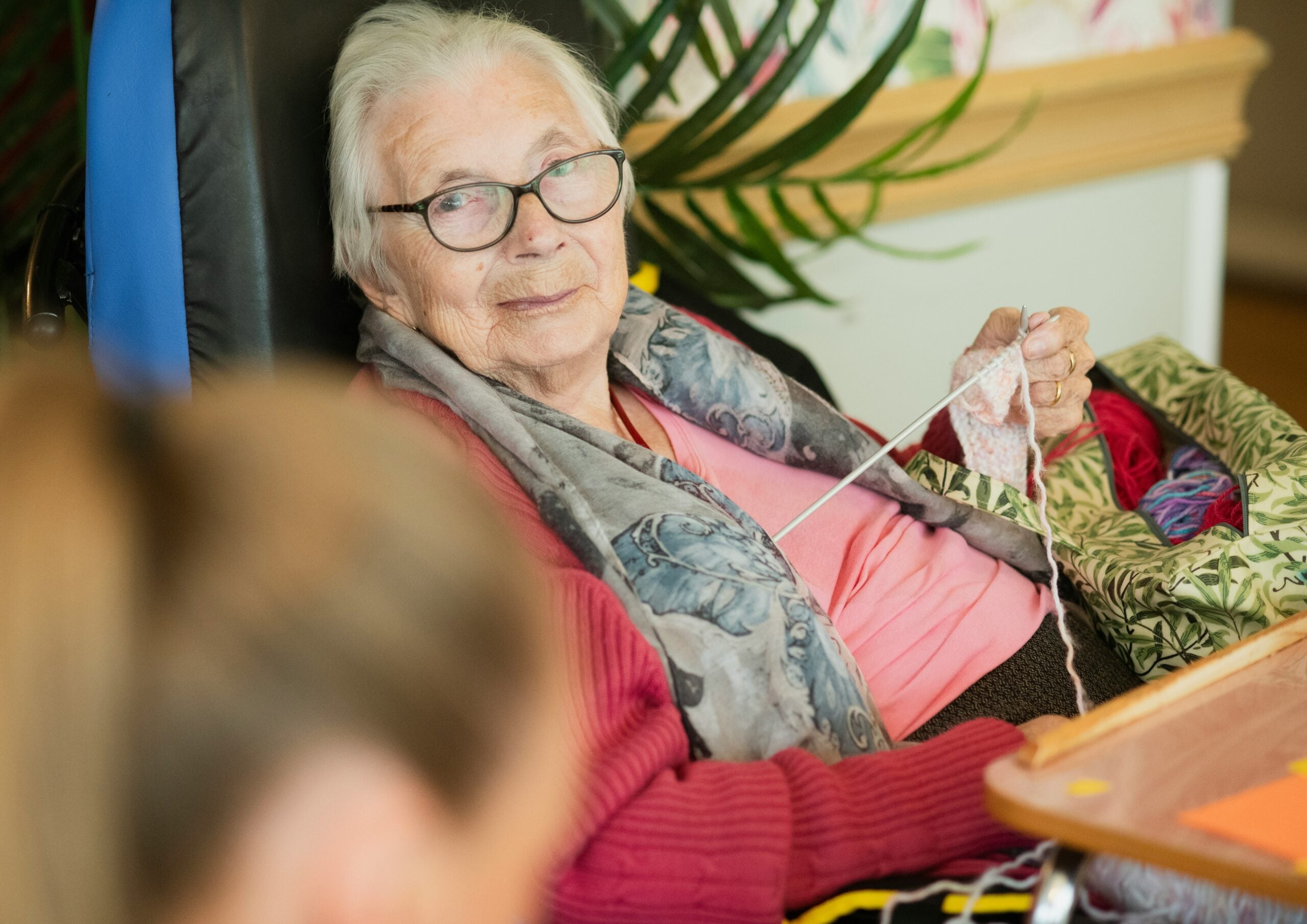 Older woman knitting at home while receiving companionship and support