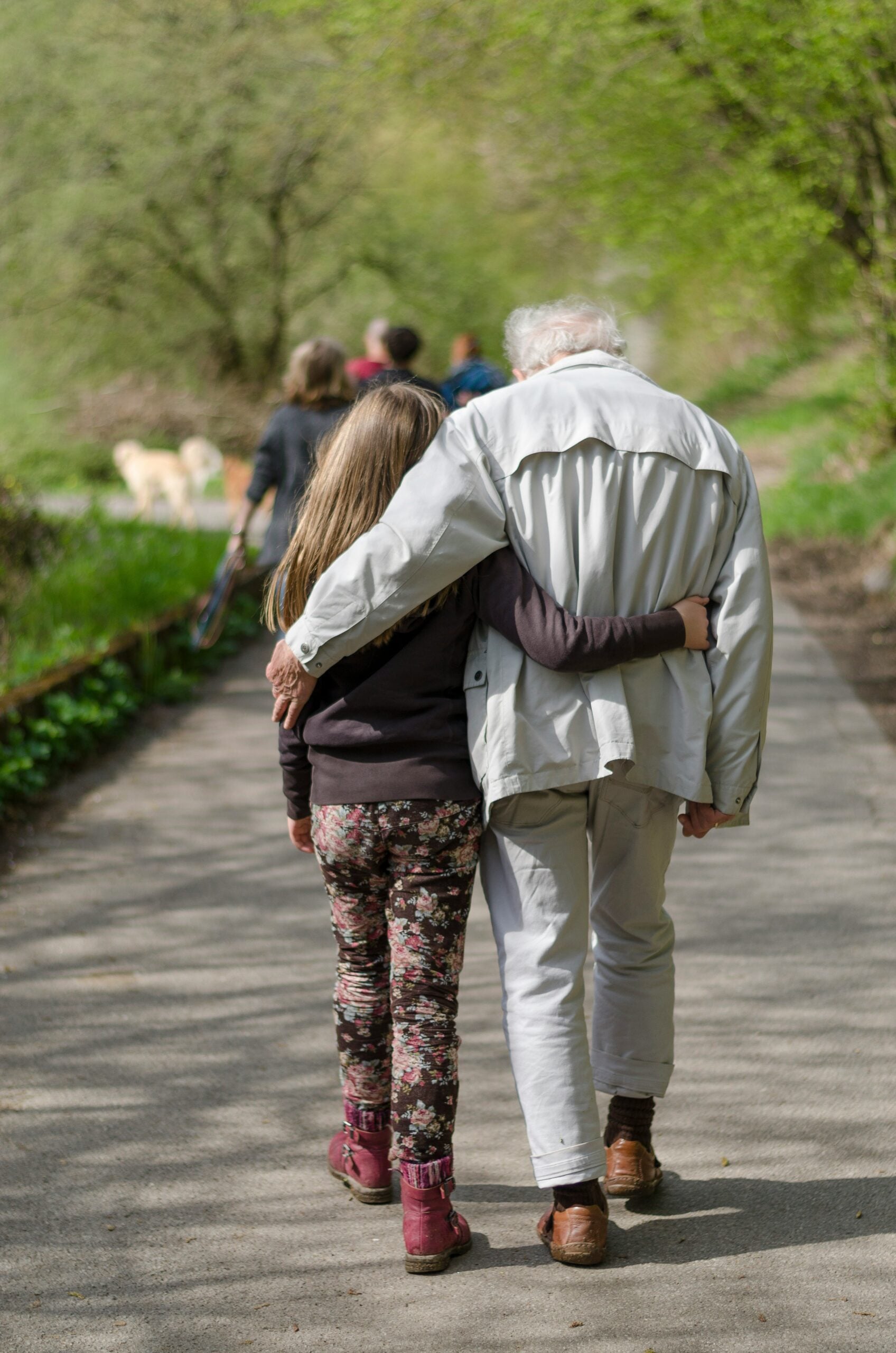 Grandfather and granddaughter walking together outdoors with their arms around each other on Grandparents Day