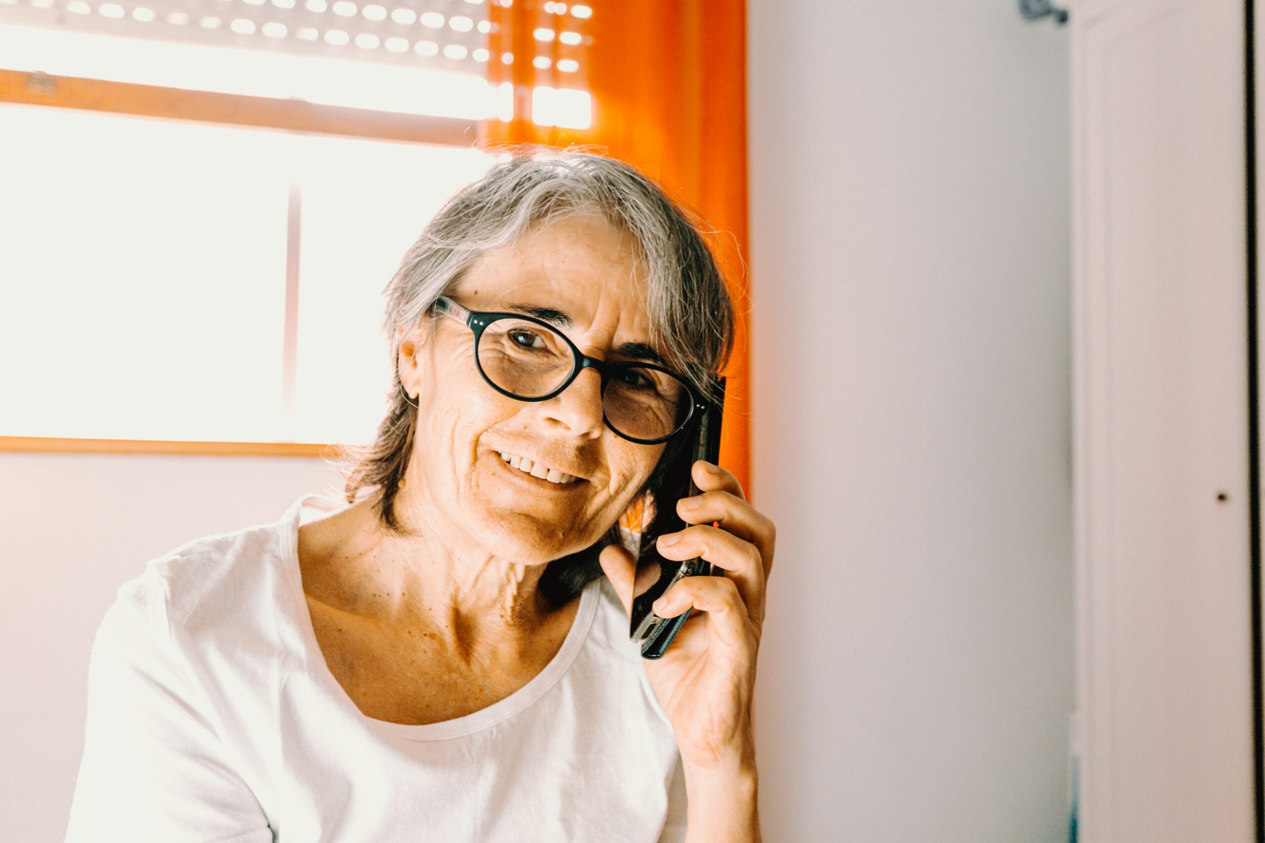 Senior woman talking on the phone at home, highlighting long-distance caregiving and home care in Naples, Florida.