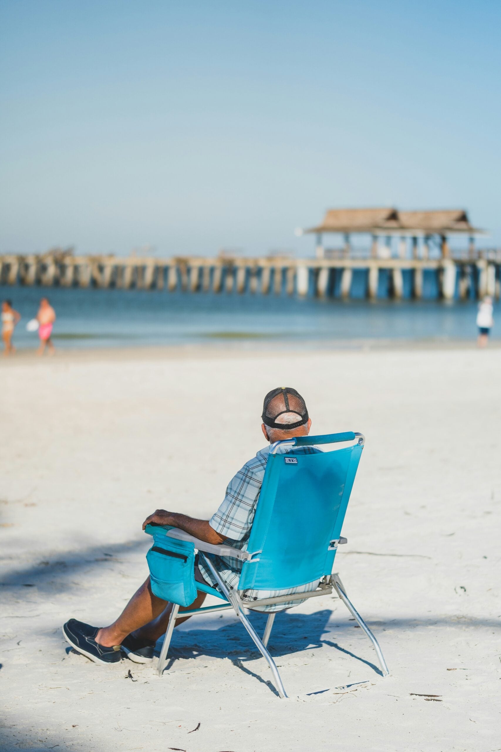 Older man relaxing in a beach chair on the white sand near Naples Pier, enjoying the sunshine in Southwest Florida.